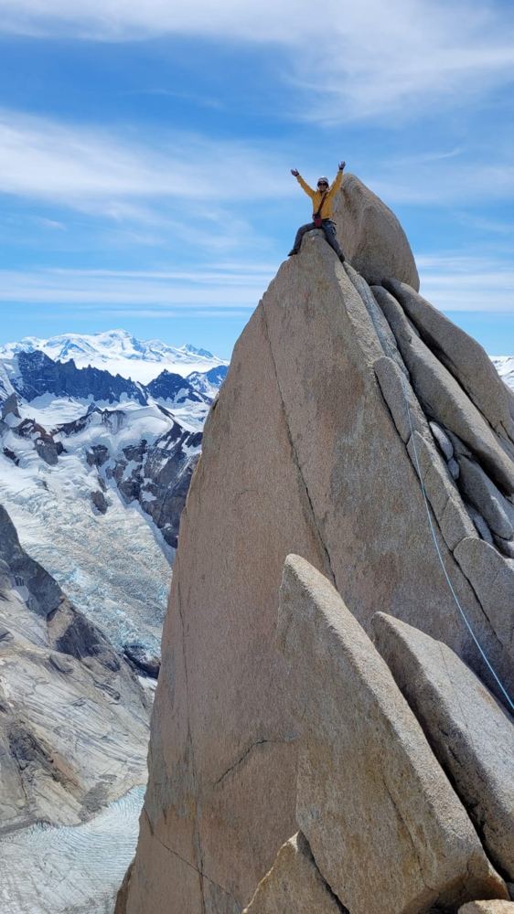 Luiza no cume de uma agulha de granito, com glaciares ao fundo